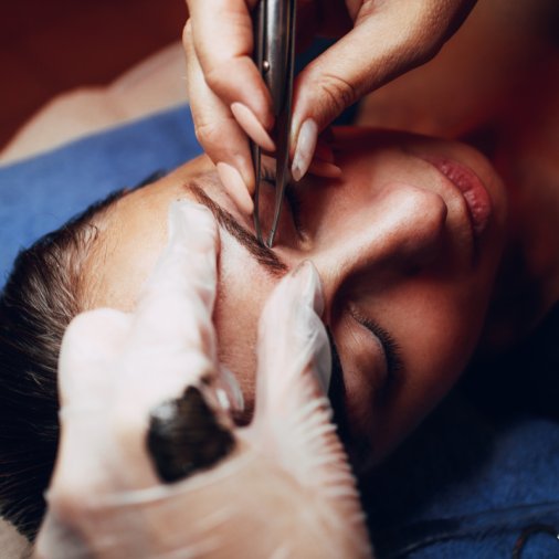 Close up of a beautician hands shaping eyebrows with tweezers to model.
