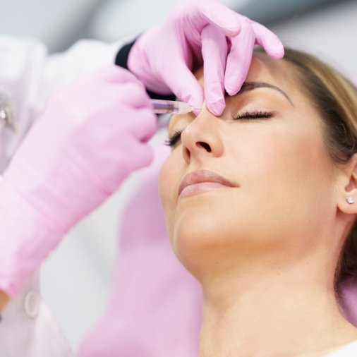 Doctor performing rhinoplasty by injection of hyaluronic acid in the nose of his patient, a middle-aged woman.